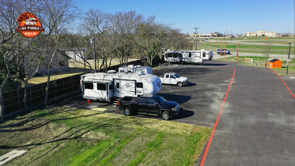 Fifth-wheel trailer and pickup trucks on paved sites along a fence at Dallas Melissa RV Park